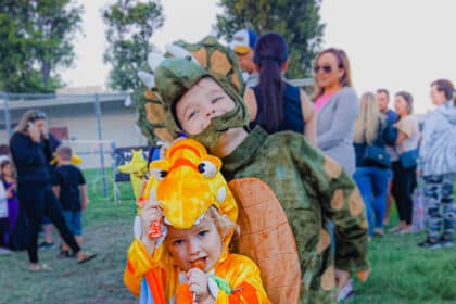 two young kids dressed in Halloween costumes. One smiles while one licks a lollipop