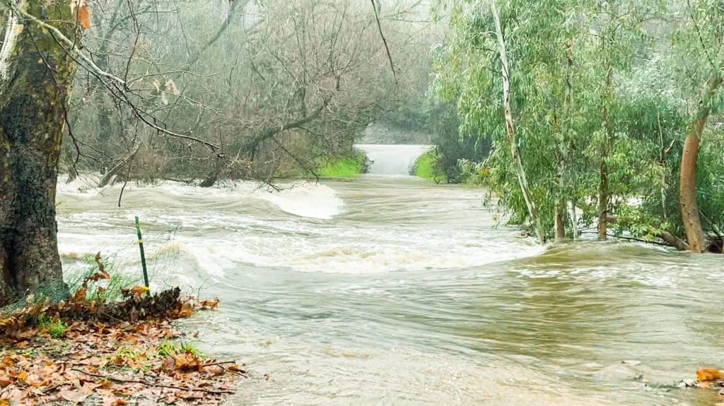 Rural county road is submerged below a raging river that is normally a seasonal dry creek. Storm Water.