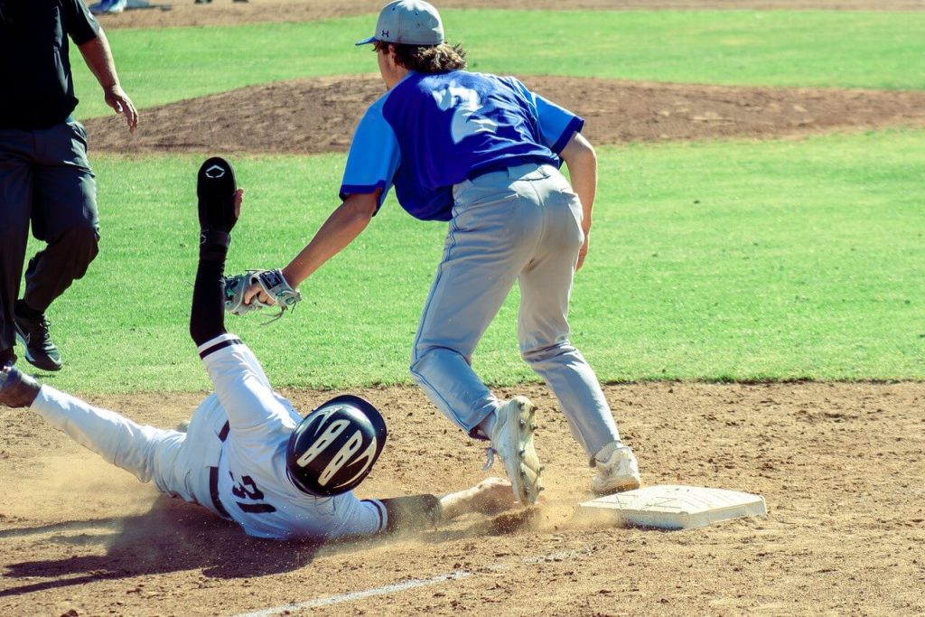 With Calabasas’ go-ahead run having just crossed the plate, Norco 3rd baseman Steven Jones reaches to apply the tag on the raised hand of the Coyotes Tyler Triessl, whose right hand is still inches from the bag. It was ruled no-tag, opening the floodgates in the bottom of the 5th. Credit: Photo by Connor Forbes