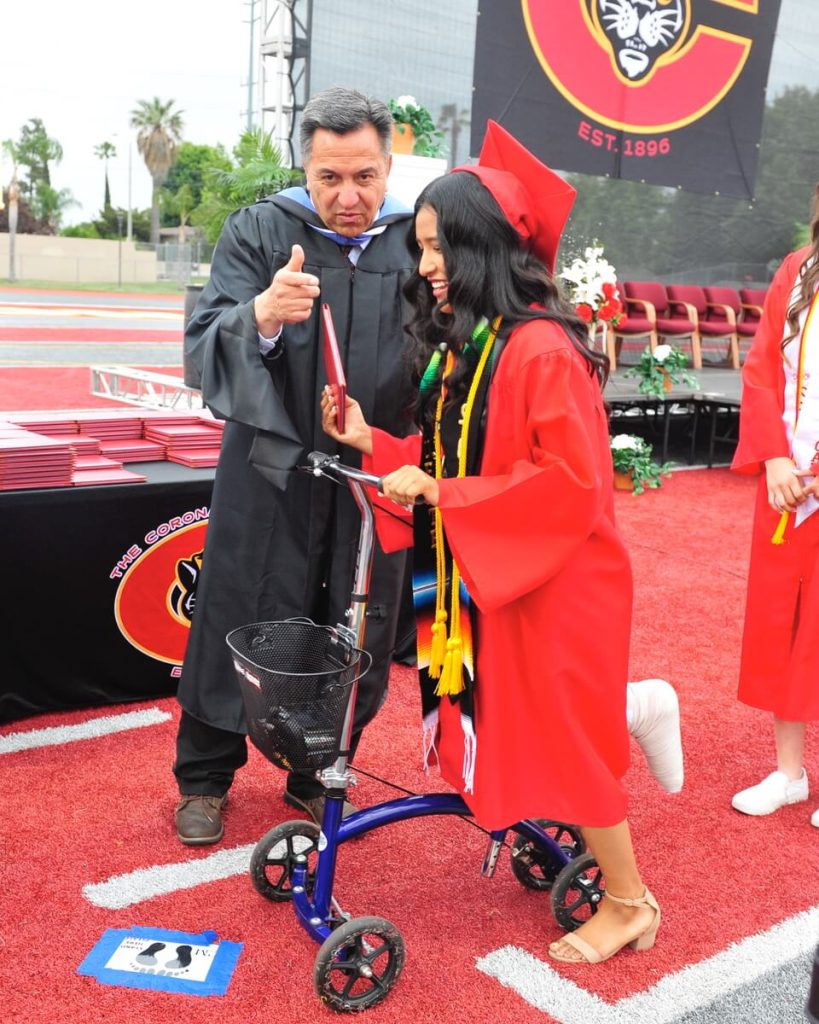 Corona High Principal Ben Sanchez gives a thumbs up to graduating senior Jazmin Carlos who uses a cart to support her broken foot.