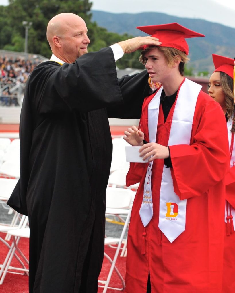Corona auto shop teacher Robert Mauger Jr. straightens the cap on graduate Andrew Roberts Jr..