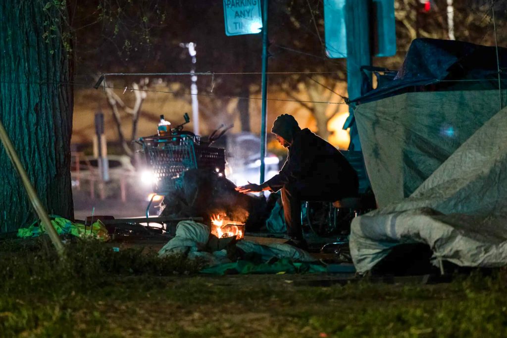 Muhammad, who declined to provide his last name, warms his hand at a fire near his tent in Sacramento. 
Credit: Photo by Miguel Gutierrez Jr., CalMatters
