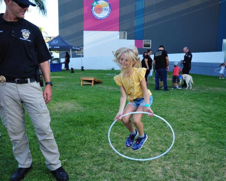 Haley Siemer, the daughter of Corona Police Cp. Russell Siemer, jumps through a hula-hoop as her father watches at National Night Out in 2022. This year’s Night Out with Corona PD takes place this coming Tuesday.
