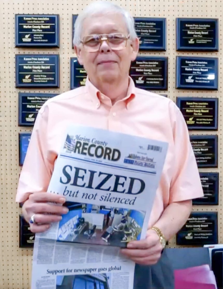 Newspaper Raid. Flanked by scores of Kansas Press Association Awards, Marion County (KA) Record Publisher Eric Meyer holds this week’s paper with the Page 1 Headline, “SEIZED…but not silenced.”
