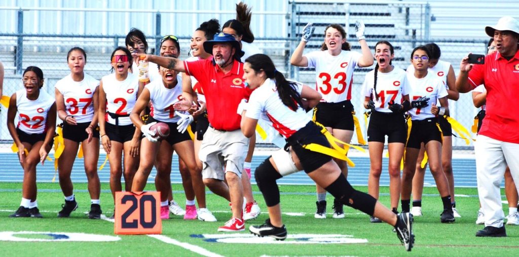 Featured Photos for the week of 9-15. Corona Coach Jim Bowers (middle) points to the end zone after Ava Liaga (center) intercepted a Santiago pass, which then set up Victoria Aguilar’s winning touchdown pass to Kristen Dizon for the Panthers. Janella Ortiz (22), Kiem-Ai Pham (37), Alexa Ramos (2), Jestinah Solomua (1) Kaelyn Rincand (33), Jaelyn Sparks (17), and Sienna Romero (7) celebrate the theft. An assistant coach catches the action on his cell phone. The Panthers defeated the Sharks 20 – 13. Photo by Gary Evans