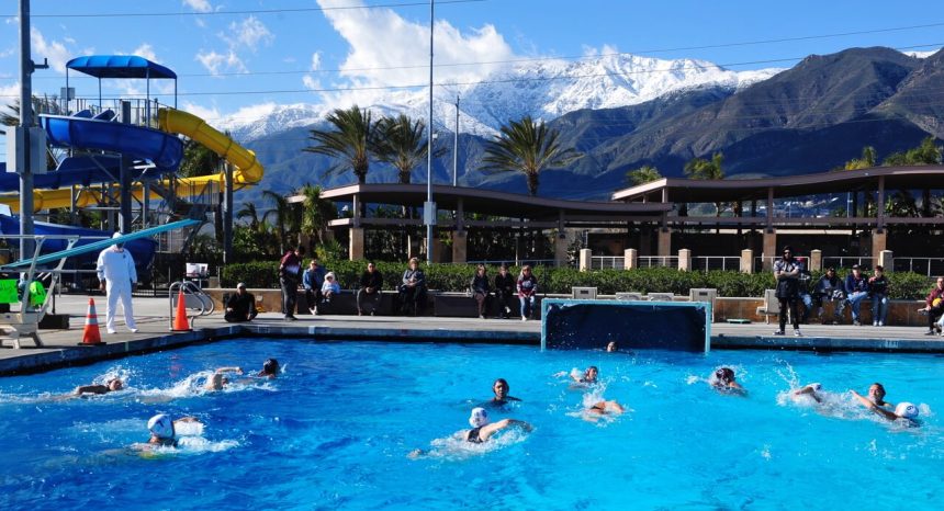 Corona Santiago and Fontana water polo competitors splash under blue skies, framed by the snow-capped San Gabriel Mountains. The sun shone on the Sharks in the 17-5 playoff win. Credit: Photo by Jerry Soifer