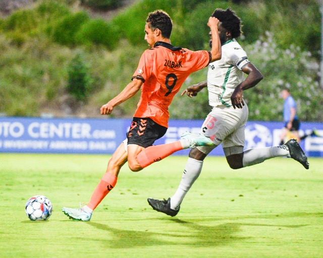 Featured Photos 7-5-24. Corona Santiago High graduate Ethan Zuback, a forward on the Orange County Soccer Club fires a shot against Oakland's Irakoze Donasiiyana in a USL game Saturday at Great Park in Irvine. Zuback missed the shot and Oakland won, 2-0. Credit: Photo by Jerry Soifer