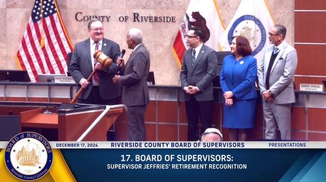 Supervisor Chuck Washington presents retiring Supervisor Kevin Jeffries with a three-foot gavel, recognizing his years of decorum and service. Supervisors Yxstian Gutierrez, Karen Spiegel and Manuel Perez (l-r) look on.