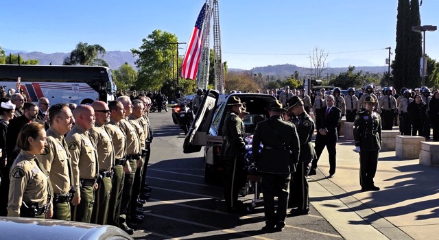 Riverside County Sheriff’s Department leadership including Sheriff Chad Bianco and other law enforcement officers and deputies stand at attention as the casket containing the remains of Motor Deputy Timothy Corlew is removed from the hearse and readied to be taken into Harvest Christian Fellowship for the memorial service.