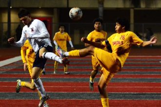 The extended left legs of Roosevelt’s Dominic Fritgez (left) and Corona’s Andrew Cortez (26) meet each other as the ball soars above. Corona’s Micah Bejarano (6) and Johan Trujillo (21) look on.