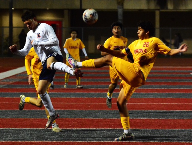 The extended left legs of Roosevelt’s Dominic Fritgez (left) and Corona’s Andrew Cortez (26) meet each other as the ball soars above. Corona’s Micah Bejarano (6) and Johan Trujillo (21) look on.