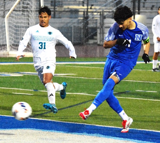 Caption: Norco’s Abraham Garcia (11) punches in his rebound for a goal off a penalty kick after Santiago goalie Gabriel Mateos blocked it.  Isaiah Guieb (31) watches the score.  Playing in a driving rain all game, the Cougars defeated the Sharks 2 – 0 in the first round of the CIF playoffs. 
Credit: Photo by Gary Evans
