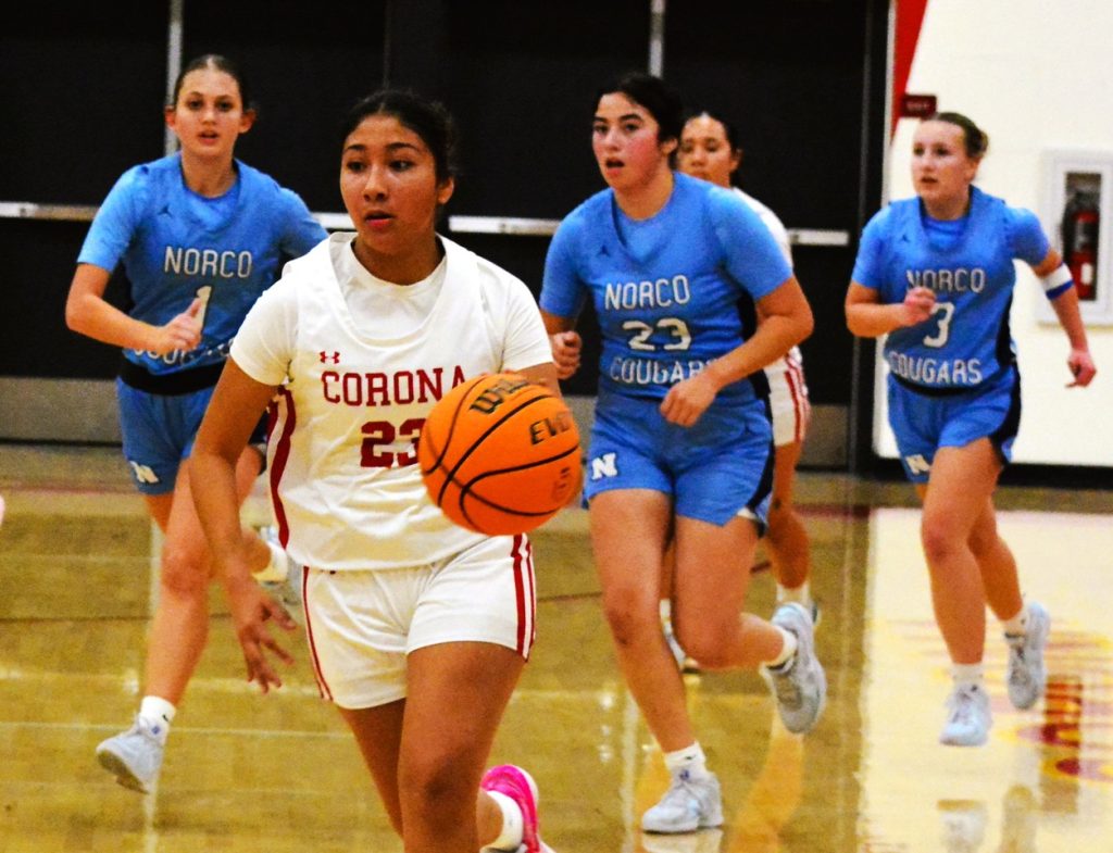 Featured Photos 02-07-2025. Corona’s Alex Flores (23) heads for a layup while Norco’s Aaliyah Taylor (1), Diana Castaneda (23) and Amber McClain (3) pursue.