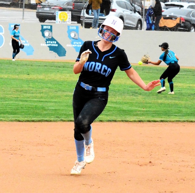 Norco’s Dakota Potter is all smiles after she blasted the ball to the centerfield fence and chugs into third with a stand-up triple.  Santiago’s Alyssa Alvarez (left) and Natalie Motto (17) work on the relay throws back to the infield.  Norco took a 4-0 lead into the top of the seventh, when Santiago rallied to tie the game.  Tamryn Shorter blistered a leadoff walk-off home run in the bottom of the seventh to give Norco the 5 – 4 victory.  
Credit: Photo by Madison Costanzo
