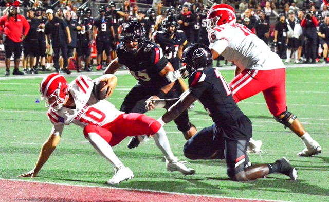 Mater Dei QB Ryan Hopkins (10) keeps from falling into the end zone for a safety after being hit by Centennial’s Jonathan McKinley II (right).  Linebacker Lucky Schirmer (55) is about to keep Hopkins at the one-yard line.   Two plays later, Hopkins fumbled the ball in the end zone, McKinley and Hopkins’ feet squibbed the ball out of the back of the end zone which gave the Huskies a 33 – 7 lead.  
