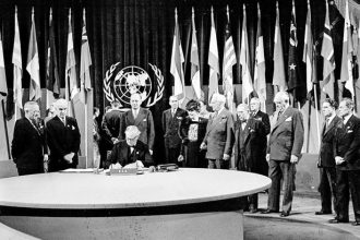President Harry S. Truman and the entire American delegation look on as Sen. Tom October 24. Connally signs the United Nations Charter in San Francisco, June 26, 1945. Standing, from left: President Truman; Secretary of State Edward Stettinius Jr.; Harold Edward Stassen; unidentified; Dean Virginia Gildersleeve; Rep. Charles A. Eaton; Rep. Sol Bloom, and Sen. Arthur Vandenberg.  Credit: AP Photo