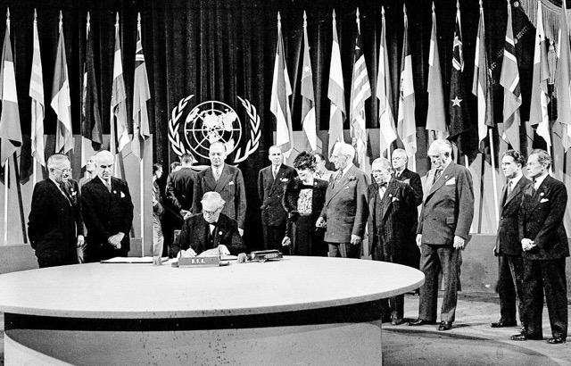 President Harry S. Truman and the entire American delegation look on as Sen. Tom October 24. Connally signs the United Nations Charter in San Francisco, June 26, 1945. Standing, from left: President Truman; Secretary of State Edward Stettinius Jr.; Harold Edward Stassen; unidentified; Dean Virginia Gildersleeve; Rep. Charles A. Eaton; Rep. Sol Bloom, and Sen. Arthur Vandenberg.  Credit: AP Photo