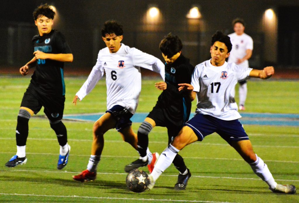 Corona Santiago’s Edgar Regalado (left) watches teammate Nathan Navarijo (center) get sandwiched by Roosevelt’s Eduardo Nuno (6) and Jason Hernandez (17) during the Sharks’ 2 – 1 win over the visiting Mustangs.