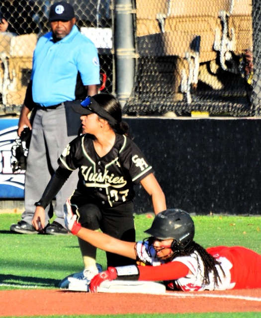 South Hills 3rd baseman Sophia Mendez (77) looks hopefully at the umpire, but Centennial’s Alanah Cole (right) hugs the bag and calls for time after being called safe. The Huskies won 7-3.