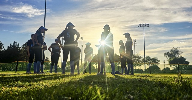 Silhouetted against the setting sun, Norco High softball players prepare for the championship game against Fullerton.