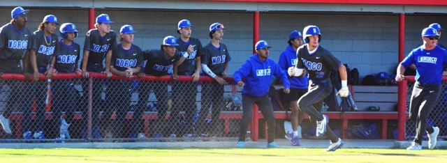The Norco bench, coaches, and runner Codey Brown (10) look to see where the ball is in the outfield as Brown heads for home and upends Panther catcher Jesiah Andrade to score.