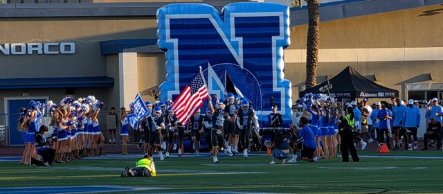 Bearing the American Flag, Norco’s Trevor Schneider leads Norco teammates and the cheer squad onto the home turf, kicking off the 2026 football season versus neighboring rival Eastvale Eleanor Roosevelt.
Credit: Photo by Gary Evans